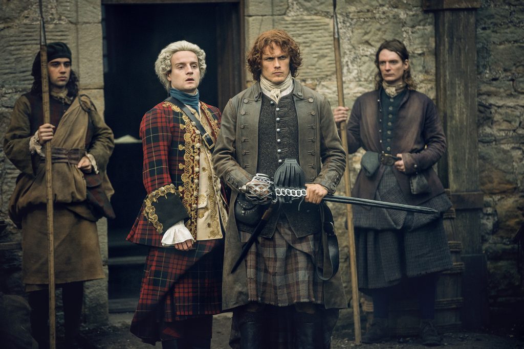 Guard 1: Dude, is he rubbing Fraser's back? Guard 2: Idk, just...just stand there and guard stuff. (Center right, Sam Heughan as Jamie Fraser.)